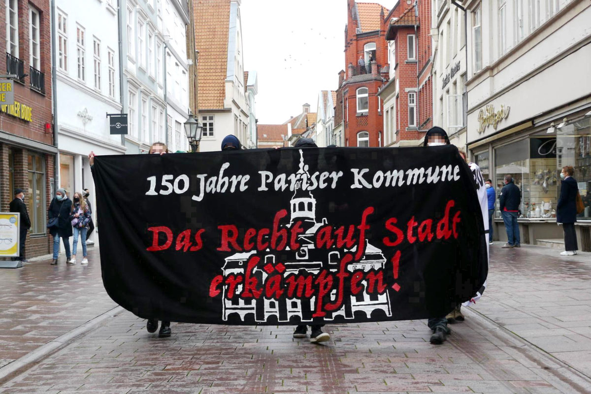Menschen mit Banner 150 Jahre Pariser Kommune - Das Recht auf Stadt erkämpfen in der Bäckerstrasse Lüneburg