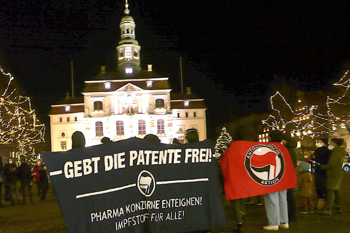 Banner: "Gebt die Patente frei!" vor dem histrischen Rathaus Lüneburg, Antifa Fahne daneben