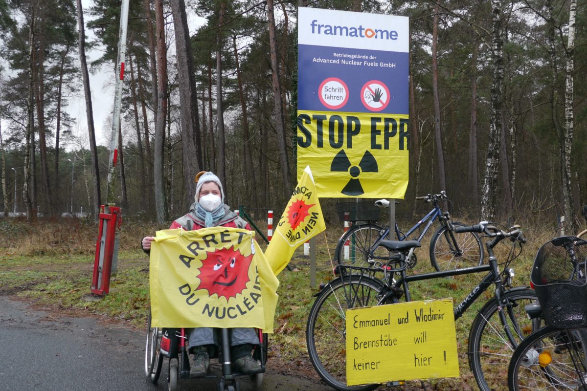 Demonstrantin mit antiatom fahne auf französisch vor einem Schild der Firma Framatome, darunter ist eine Stop EPR mit AKW logo angebracht