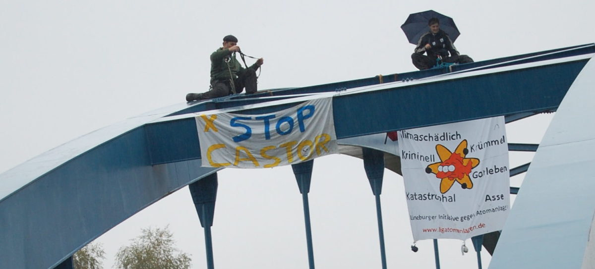 zwei Personen mit Regenschirm und antiatom banner auf einer Brücke