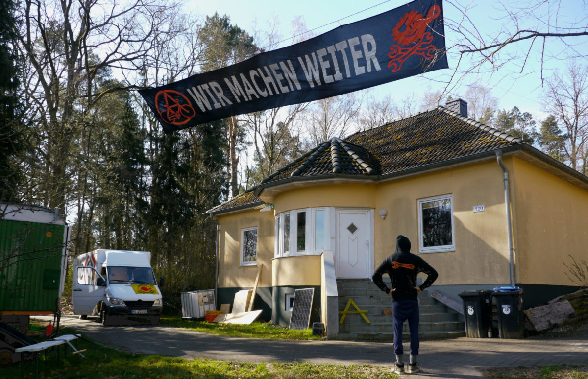 Banner Wir machen weiter mit einem Anrchie A und FAhrrd udn Trainstopping antiatom Logo . vor einem Haus