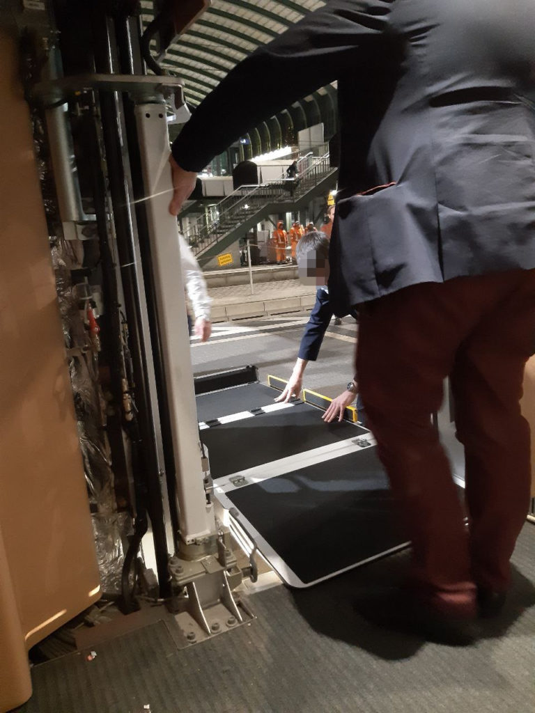 der Lift wurde befreit, das Zugpersonal versucht diesen einrasten zu lassen, im Hintergrund gucken Bauarbeiter amüsiert zu. Bild vom Inneren des Zuges aus Aufgenommen