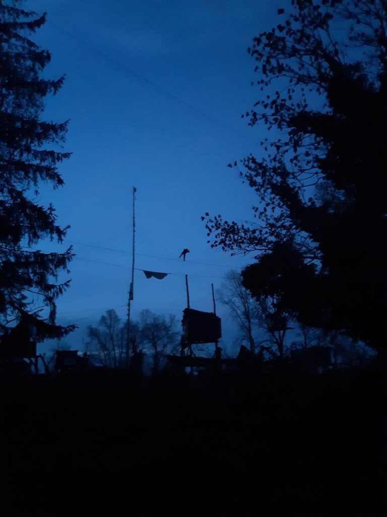 blauer abendhimmel, Bäumen, Monotpod und Seile dazwischen, eine person klettert in den Seilen