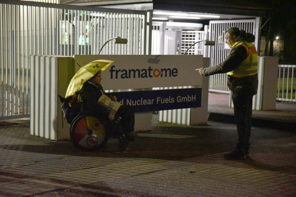 Rollstuhlfahrerin vor dem Schild Framatome ANF und Polizist mit Zeigefinger zu ihr